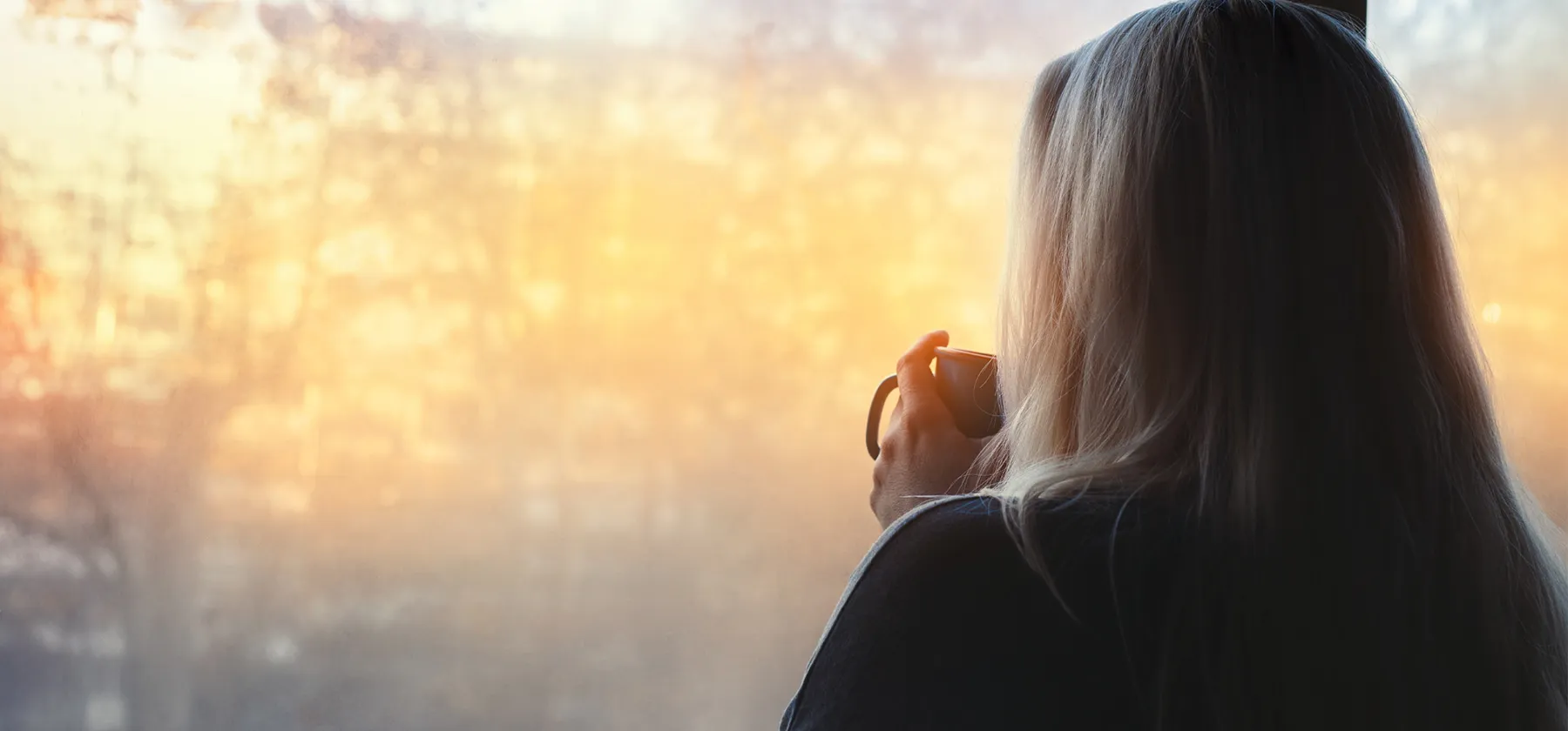 A person in quiet reflection by a window in soft morning light