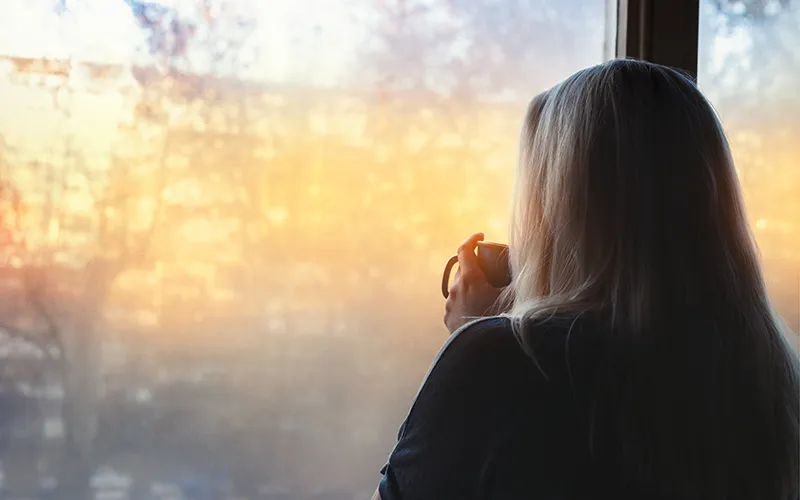 A person in quiet reflection by a window in soft morning light